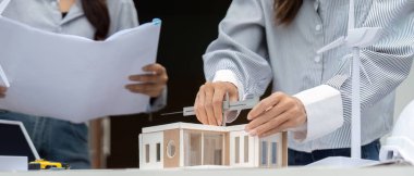 İki mimar sürdürülebilir tasarım, bir model binayı incelemek ve yenilenebilir enerji seçeneklerini tartışmak, çevre dostu mimarinin önemini vurgulamak için işbirliği yaparlar..