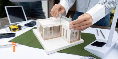 Sürdürülebilir bir yapı modelini ölçmek için kalibreleri kullanan bir mimarın yakın plan çekimi, çevre dostu tasarımda hassasiyetin önemini vurguluyor.