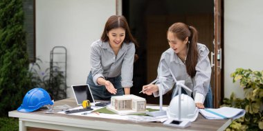 İki mimar sürdürülebilir mimari üzerinde işbirliği yapar, bir yapı modelini inceler ve rüzgar türbinleri gibi çevre dostu tasarım unsurlarını tartışırlar..