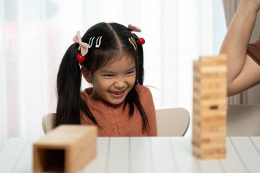 Memnun bir kız, Jenga 'daki başarılı hamlesini kutluyor. Heyecanını ve annesiyle oynadıkları oyun sırasında kurduğu neşeli bağı gösteriyor..