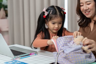 Bir çocuk okul için ebeveynin yardımıyla sırt çantalarını düzenleyerek hazırlanır ve eğitime hazırlanmanın önemini vurgular..