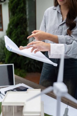 İşbirlikçi bir ortamda, iki profesyonel sürdürülebilir yapı planlarını analiz ederek, çevre dostu uygulamaları ve tasarımlarındaki yenilenebilir enerji entegrasyonunu vurguluyor.