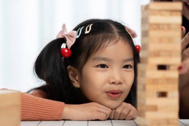 Kız eğildi, Jenga oyununa odaklandı, annesiyle oynadığı eğlenceli öğrenme deneyiminde kararlılığını ve neşesini gösterdi..