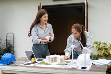 İki mimar, bir model ve rüzgar türbinleri gibi çevre dostu özellikleri tartışarak sürdürülebilir yapı tasarımları üzerinde işbirliği yapıyorlar..