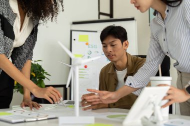 Beyin fırtınası yapan dinamik bir ekip, rüzgar türbini modelleri ve sürdürülebilirlik çabalarını geliştirmek için görsel araçlarla ESG stratejilerini tartışıyor..