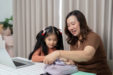 Neşeli bir anne kızının okul çantasını toplamasına yardım eder, okula dönüş hazırlıkları için pozitif ve destekleyici bir ortam yaratır..