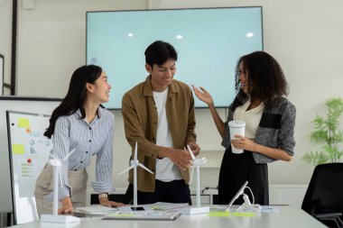Genç bir profesyonel takım rüzgar teknolojisi modelleri üzerinde tutkuyla beyin fırtınası yapıyor, sürdürülebilir uygulamalara olan bağlılıklarını kurumsal bir ortamda somutlaştırıyorlar..