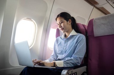 İçerik sahibi bir iş kadını, pencerenin önünde otururken bilgisayarına yazar, işine dalmış ve uçuş deneyiminin tadını çıkarır..