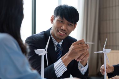 Bir adam, rüzgar türbini modelleri kullanarak sürdürülebilir enerji çözümleri hakkında meslektaşlarına danışıyor ve toplantılarında ESG stratejilerini geliştiriyor..