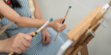 Bir anne, resim fırçalarını bir arada tutarken kızına destek olur, yaratıcılığı ve takım çalışmasını teşvik eder..