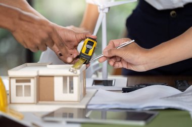 Sürdürülebilir inşaat, sergilenen takım çalışması ve yenilikçi tasarım planlaması için bir model evi ölçen mühendisler.