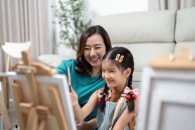 Birlikte resim yapan bir anne ve kız arasında paylaşılan neşeli bir an, sanat oturumları sırasında yaratıcılık ve kahkahaları ifade ediyor..