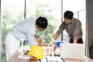 Mühendisler, modern bir ofiste sürdürülebilir uygulamaları tartışırken, çevre dostu mimari modeller tasarlıyorlar..