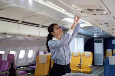 Bir uçuş görevlisi dikkatle uçaktaki kompartımanı ayarlıyor, iş seyahati sırasında yolcu konforu ve güvenliğini sağlıyor..