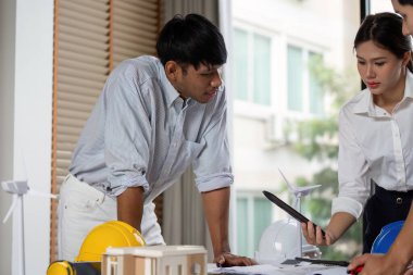 Mühendisler, sürdürülebilir tasarım ve takım çalışmasını destekleyen, bir masa üzerindeki proje planları hakkında bir tartışmaya giriştiler..
