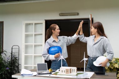 İki sürdürülebilirlik mühendisi takım çalışmalarını ve projelerini dışarıda tamamlamayı kutluyor, beşlik çakıyor ve çevre dostu tasarımlarını tartışıyorlar..