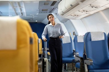 Bir hostes, iş seyahati sırasında göstermiş olduğu özen göstererek, bavullarını taşıyan genç bir bayana yardım eder..