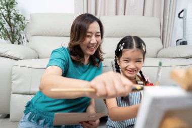 Neşeli bir anne ve kız birlikte resim yaparak eğleniyorlar, ev ortamlarında yaratıcılığı teşvik ediyorlar..