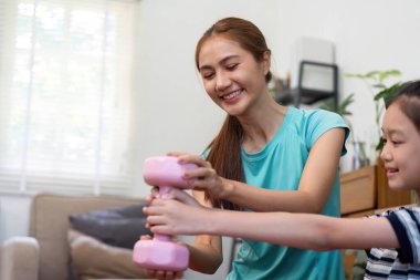 Neşeli bir anne, kızının evde pembe ağırlıkları kaldırmasına yardım ediyor. Zindelik ve sağlıklı yaşam tarzı seçimleriyle sağlığını ve bağlılığını destekliyor..