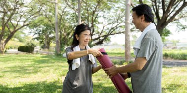 Yoga antrenmanına katılan neşeli, kıdemli bir çift birbirlerine gülümserken ortak aktivitelerinde iletişim ve sağlıklarını gösteriyorlar..