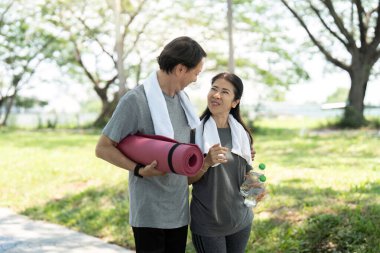 Parkta yoga yapan yaşlı bir çift ağaçların altında birlikte pratik yaparken neşe ve sağlık yayıyorlar..