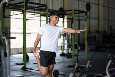 Genç bir adam bacağını uzatır, spor salonundaki esneklik ve esneme üzerine odaklanır..
