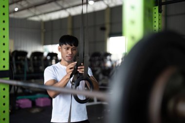 Genç bir adam spor salonu yüzükleriyle antrenman yapmaya hazırlanıyor. Rutinindeki sağlık ve zindeliğin önemini vurguluyor..