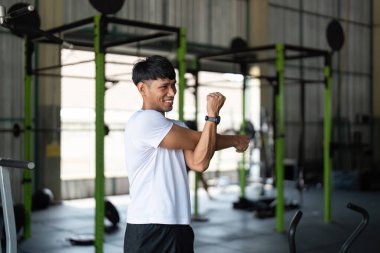 Gülümseyen genç bir adam kollarını uzatır, spor salonundaki esneklik ve esnekliği teşvik eder..