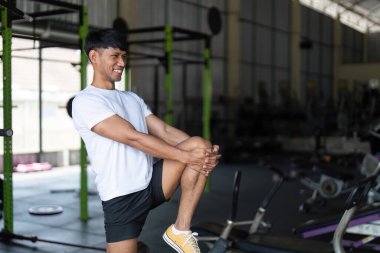 Spor salonunda bacak esneten bir adam, sağlıklı ve canlı bir çalışma ortamında fiziksel uygunluğu teşvik eder..