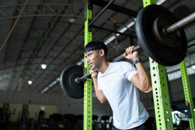 Kararlı genç bir adam halterle çömeliyor, spor salonunda güç ve sağlığa odaklanıyor..