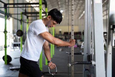Odaklanmış genç bir adam, modern bir spor salonunda sağlık ve zindeliği destekleyen bir kablo makinesi kullanarak güç eğitimine başlıyor..