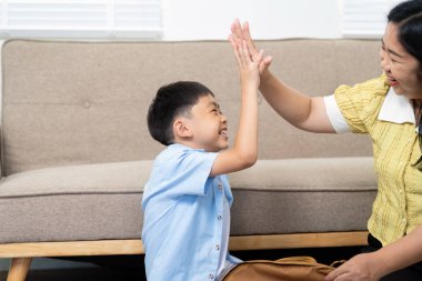 Küçük bir çocuk annesine beşlik çakarken neşeli bir an, evde öğrenme sırasında heyecan ve bağlantıyı yansıtıyor..