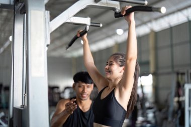 Bir kadın, modern bir spor salonunda güç ve sağlığa odaklanarak kişisel antrenörüyle antrenman yapmaktan zevk alır..