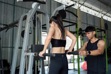 Kişisel antrenör müşteriye barfiks egzersizinde rehberlik eder. Spor salonunda sağlık ve güç eğitimini ön plana çıkarır..