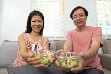 Yaşlı bir çift gururla taze salatalarını sunuyor, sağlıklı olduklarını ve sağlıklı beslendiklerini sıcak bir evde gösteriyorlar..