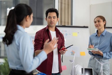 Sürdürülebilir bir enerji projesi için çeşitli mühendislerden oluşan bir grup, parlak bir ofis alanında rüzgar türbinleri ve çevre dostu tasarımlar sergiliyor..