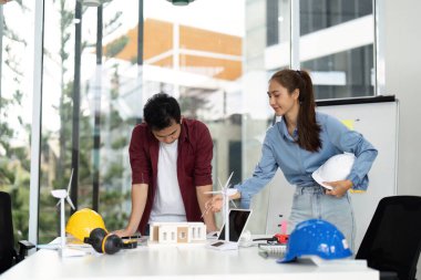 Sürdürülebilir bir enerji projesi için çeşitli mühendislerden oluşan bir grup, parlak bir ofis alanında rüzgar türbinleri ve çevre dostu tasarımlar sergiliyor..