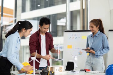 Sürdürülebilir bir enerji projesi için çeşitli mühendislerden oluşan bir grup, parlak bir ofis alanında rüzgar türbinleri ve çevre dostu tasarımlar sergiliyor..