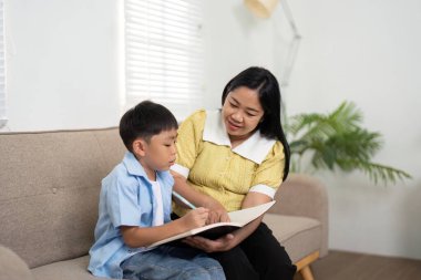 Bir anne küçük oğluna okumasında yardımcı olur, evde destekleyici bir öğrenme ortamı oluşturur..