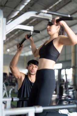Kişisel antrenör bir kadına barfiks makinesinde yardım eder, destekleyici bir spor salonundaki sağlık ve sağlık durumunu vurgular..