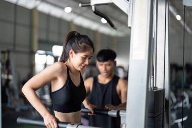 Bir kadın spor salonunda spor yaparken kendisine rehberlik eden bir antrenörle dayanıklılık eğitimi alıyor..