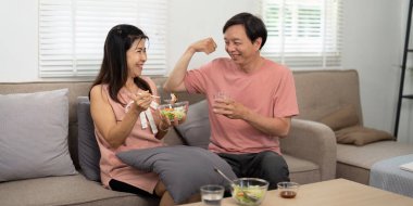 Yaşlı bir çift besleyici bir salata ve içeceği paylaşıyor, rahat oturma odalarında sağlıklarını ve bağlantılarını destekliyor..