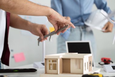 Bir mühendis, çevre dostu tasarım için hassas boyutlara odaklanarak, sürdürülebilir minyatür bir yapı modelini dikkatlice ölçer..