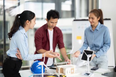 Sürdürülebilir bir enerji projesi için çeşitli mühendislerden oluşan bir grup, parlak bir ofis alanında rüzgar türbinleri ve çevre dostu tasarımlar sergiliyor..