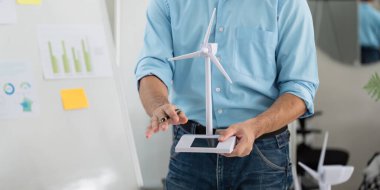 Bir iş adamı, modern bir ofiste sürdürülebilirlik ve ESG girişimlerini tartışan bir rüzgar türbini modeli tutuyor..