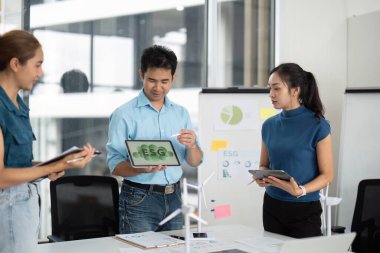Profesyonel bir ekip, parlak ofis ortamında tablet kullanarak ESG stratejileri ve yenilenebilir enerji çözümleri sunar.
