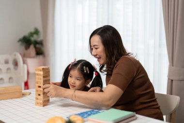 Bir anne ve kızı, sıcak bir ev ortamında Jenga bloklarını üst üste yığıp bağlarını güçlendirirken kahkaha ve neşe paylaşıyor..