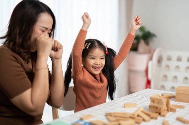 Bir anne, kızı Jenga oyununda kazandığı zaferi kutlarken gülümser. Neşeli aile anlarını vurgular..
