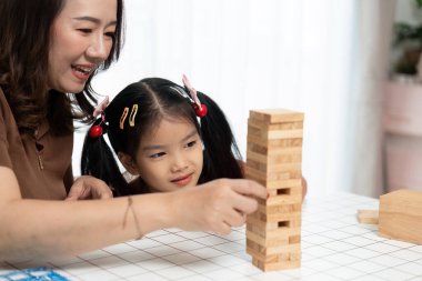 Neşeli bir anne ve kız Jenga oynarken kaynaşıyor, rahat bir yuva ortamında bağ ve yaratıcılığı teşvik ediyor..