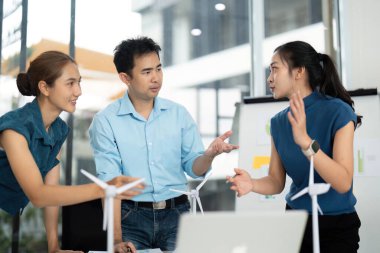 Üç profesyonel, parlak bir ofis alanında yenilenebilir enerji çözümleri ve ESG girişimleri hakkında bir tartışmaya girişti.